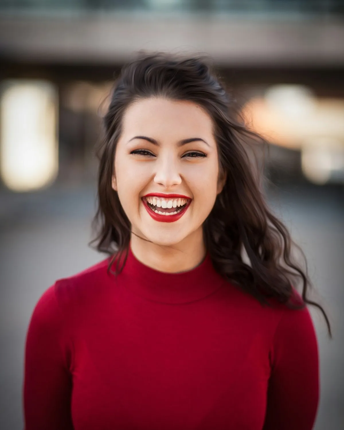 Portrait of a smiling woman with curly hair, lit by soft window light against a plain wall.