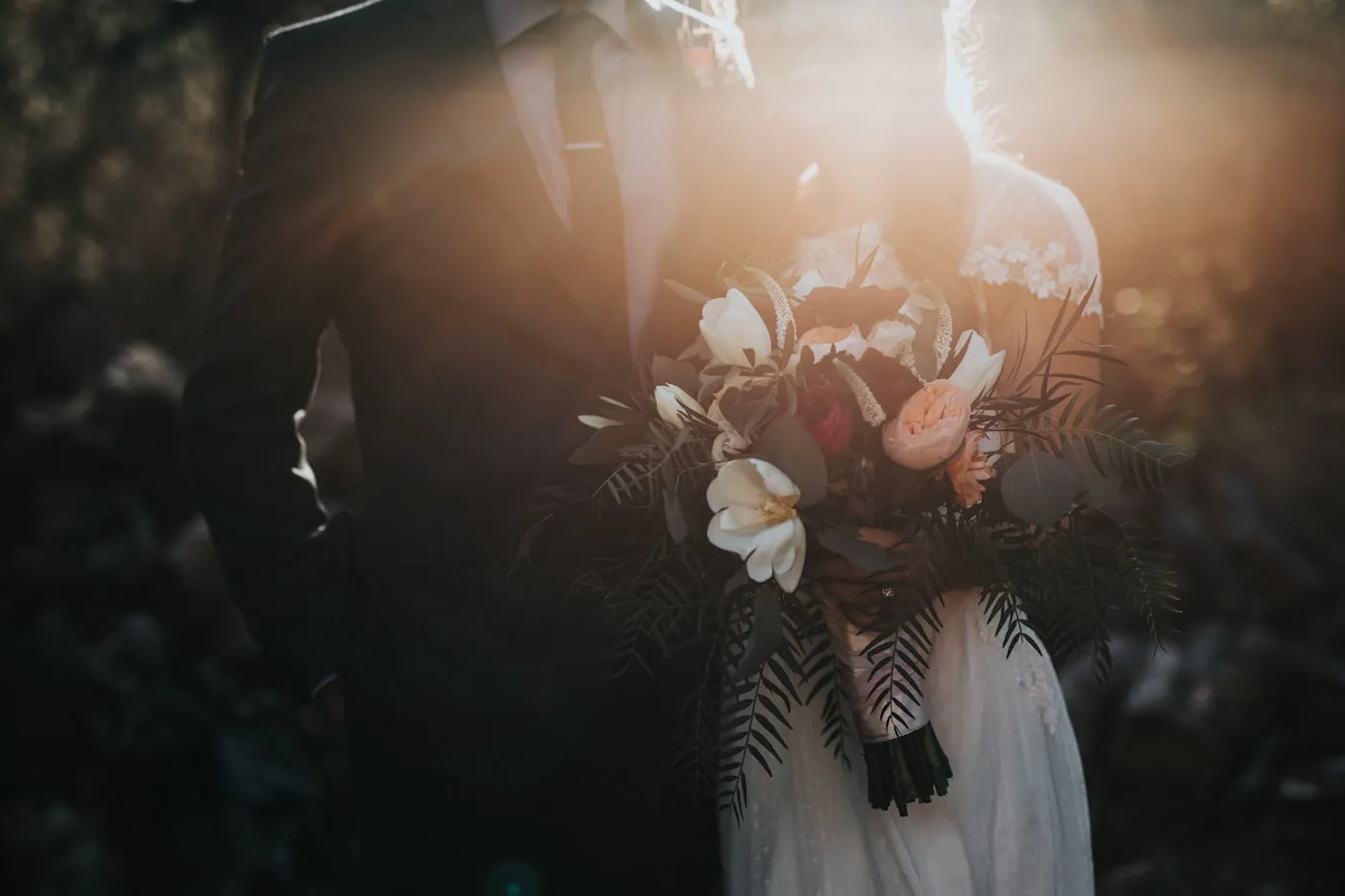 A newlywed couple walk hand in hand along a path in soft morning light.
